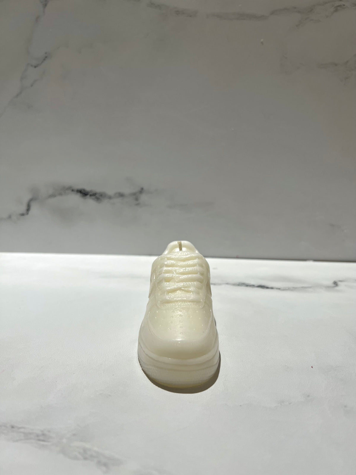 The AF1 – White Lowtop Sneaker Candle – Small (On Backorder), hand poured with Black Ice fragrance, rests on a white marble surface against a light gray marble background.
