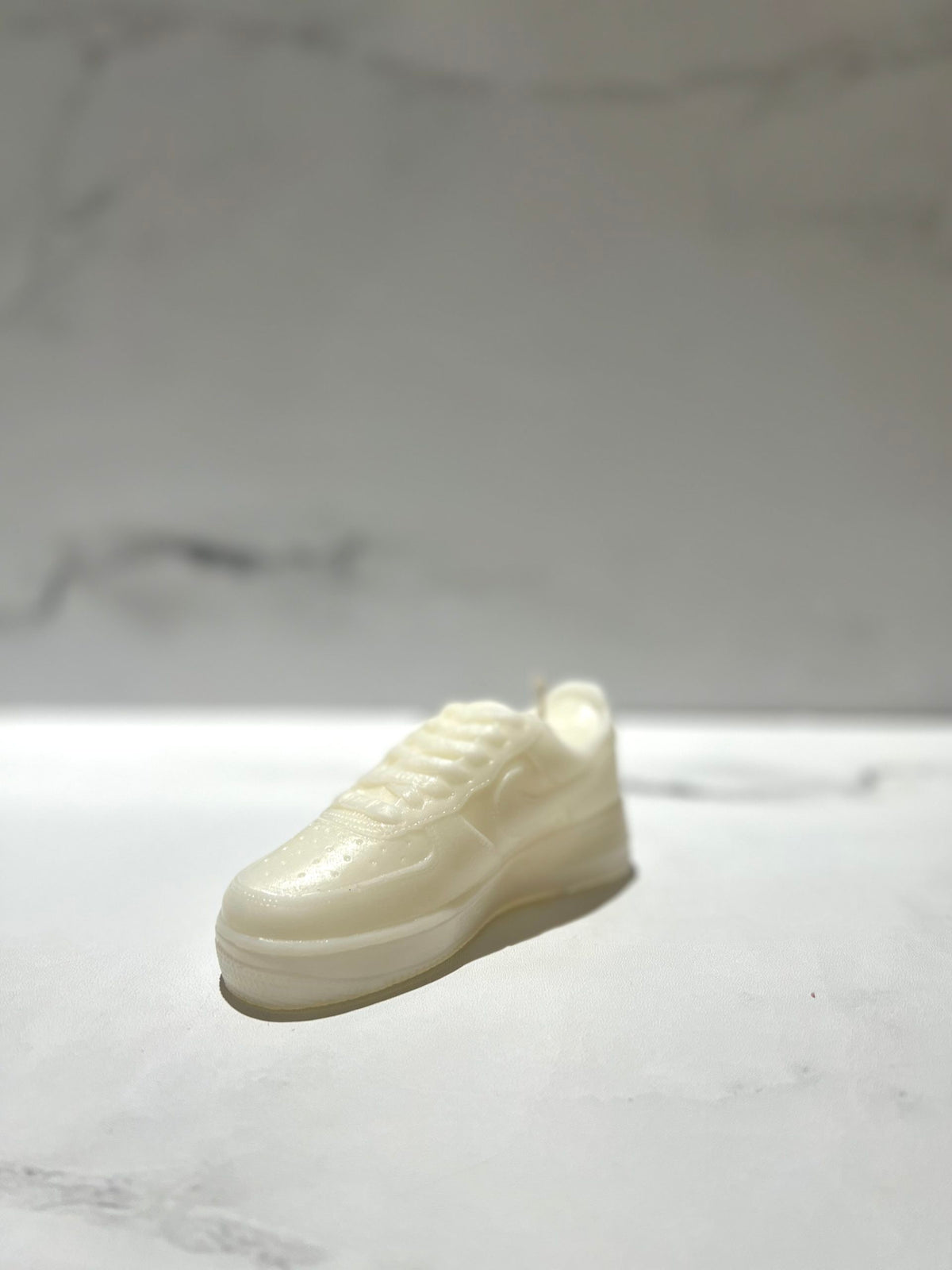 The AF1 – White Lowtop Sneaker Candle – Small (On Backorder) is a white, sneaker-shaped candle, hand-poured and infused with Black Ice fragrance, displayed on a smooth light surface with a blurred background.