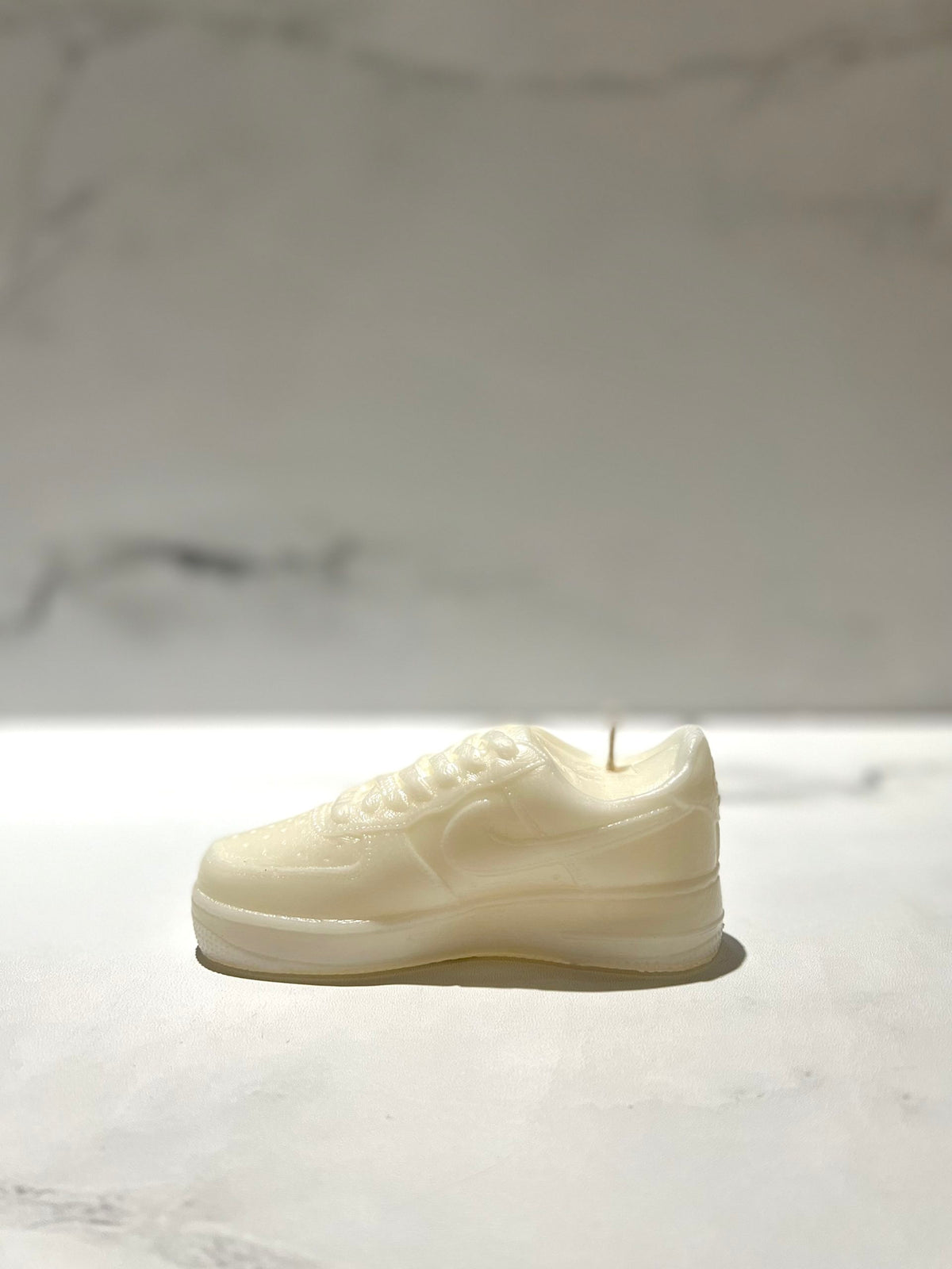 The AF1 – White Lowtop Sneaker Candle – Small (currently on backorder) is hand-poured, possibly scented with Black Ice, and shown on a light surface with a blurred background.
