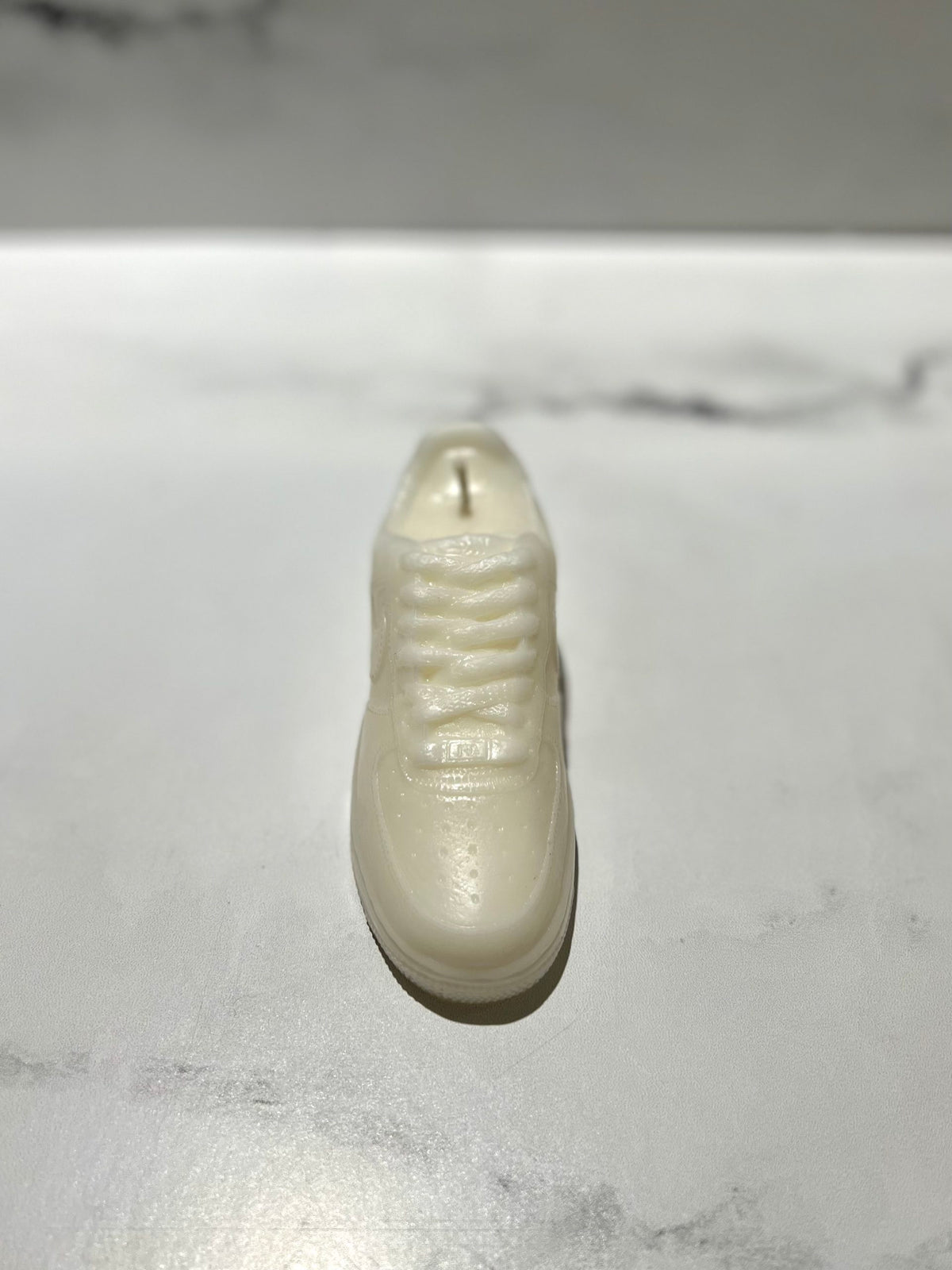 The AF1 – White Lowtop Sneaker Candle (Small, On Backorder) is hand-poured, shaped like a stylish shoe, and infused with Black Ice fragrance—adding a modern, unique touch to any space. Displayed on a light marble surface.