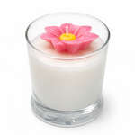 Candle in a glass container with a pink flower-shaped candle wick on a white background