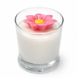 Candle in a glass container with a pink flower-shaped candle wick on a white background