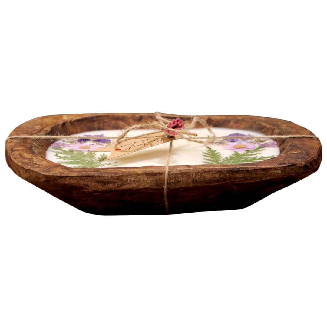 A rustic wooden bowl holds the Purple Floral Wood Candle – Floral Scented, crafted with coconut-apricot wax, adorned with pressed purple flowers and green ferns, and finished with twine and a small tag.