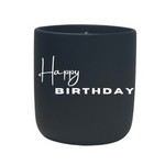 The Quoted - "Happy Birthday" Candle is a black jar made with all-natural wax and features "Happy Birthday" written in white on the front.