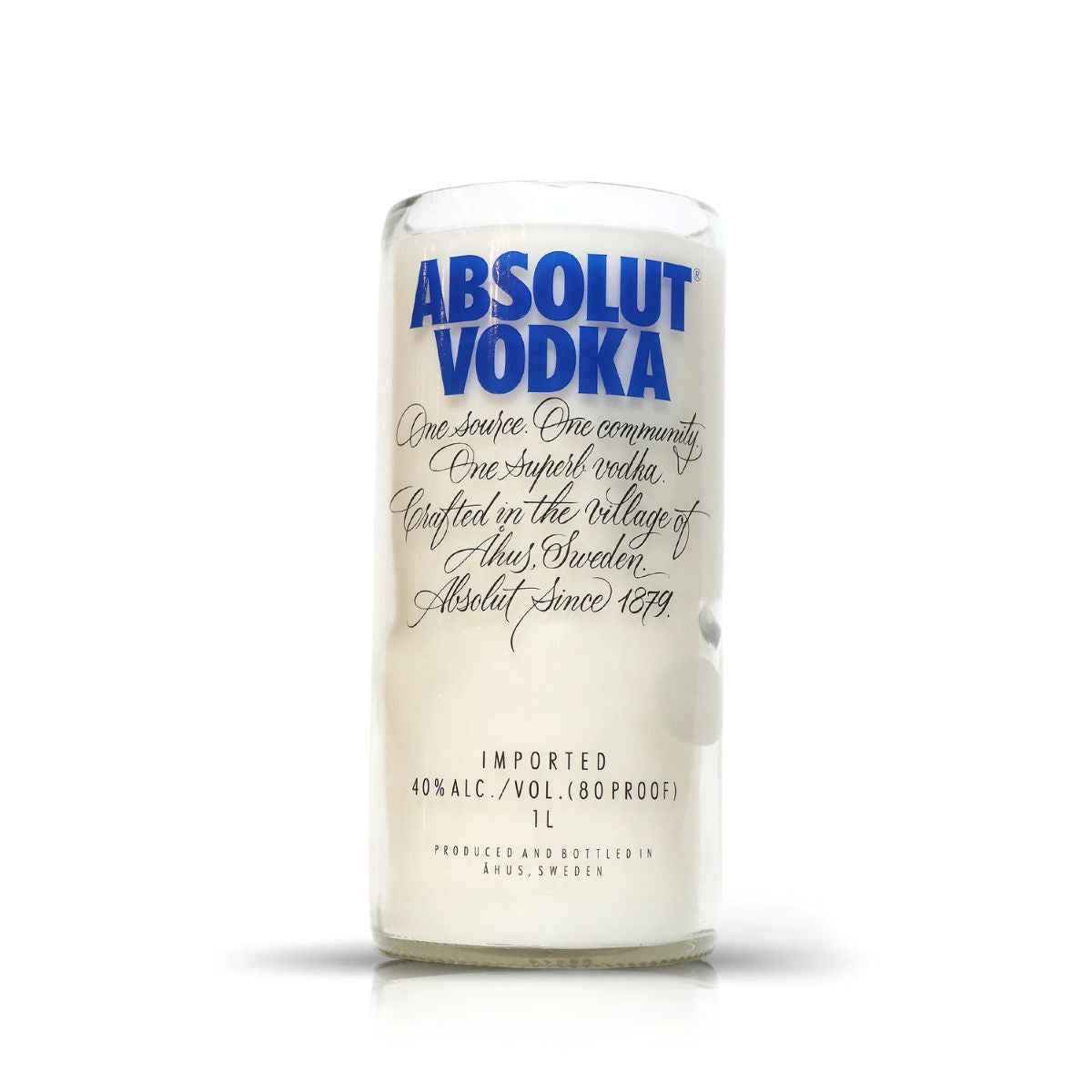 A Recycled Swedish Vodka Candle, crafted from a clear glass Absolut Vodka bottle featuring blue and black text, sits on a white background—ideal as an artisanal or eco-friendly candle.