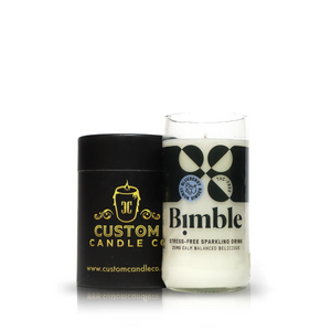 A white Recycled Sparkling Water Candle in an upcycled bottle glass sits beside a black Custom Candle Co. box on a white background, highlighting the charm of eco-friendly decor.