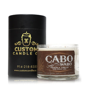 A Custom Candle Co. black cylindrical container sits next to a Recycled Azul Agave Anejo Tequila Candle, displayed in a glass bottle with brown and white design accents.