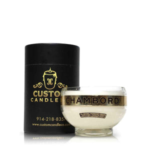 A Recycled Loire Valley Liqueur Candle made from upcycled glass, labeled "CHAMBORD," sits in front of a black cylindrical box featuring gold Custom Candle Co branding and contact info.