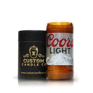 The Recycled Light Beer Candle, hand poured in a brown glass Coors Light bottle, is displayed next to a black Custom Candle Co. container on a white background.