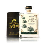 A Recycled Reserva Reposado Tequila Candle in a black cylindrical Custom Candle Co. container, made from a recycled tequila bottle, is displayed with a label featuring agave plants and product details.