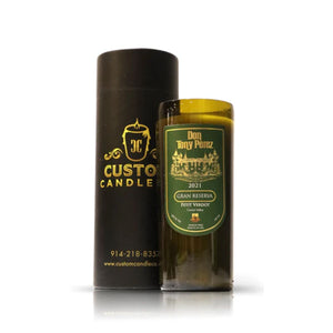 The Recycled Gran Reserva Wine Candle, crafted from recycled bottles and labeled "Don Tony Perez 2021 Gran Reserva Petit Verdot," stands beside its black cylindrical packaging, showcasing our eco-friendly approach.