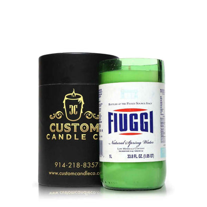 A cut green bottle labeled "Recycled Natural Spring Water Candle" stands beside a black cylindrical box, featuring an upcycled candle crafted from beverage bottles for a unique, sustainable touch.