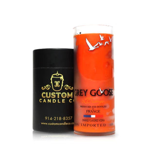 A black cylindrical Custom Candle Co. container is placed next to the Recycled French Vodka Candle - Orange, which is crafted from a repurposed vodka bottle for a unique, eco-friendly accent.