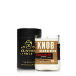 A Recycled Single Barrel Whiskey Candle, made from upcycled bottles, is displayed in front of a black Custom Candle Co. cylinder container.