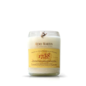 The Recycled Cognac Candle is a white candle in a glass container, made from recycled cognac bottles, and displays a Rémy Martin 1738 Accord Royal label on the front.