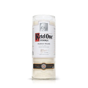 The Recycled Red Letter Vodka Candle, crafted from a vodka bottle with a white label, black and red text, and silver cap, is ideal for eco-friendly decor or as a unique recycled bottle candle displayed on any surface.