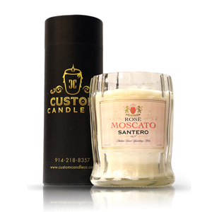 A Recycled 1958 Rose Wine Candle sits beside a sleek black container with gold "Custom Candle Co." text and contact details, showcasing their elegant upcycled wine bottle candles.