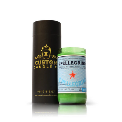 A Recycled Sparkling Natural Mineral Water Candle in a green upcycled bottle is placed beside a black cylindrical Custom Candle Co. box with gold lettering.
