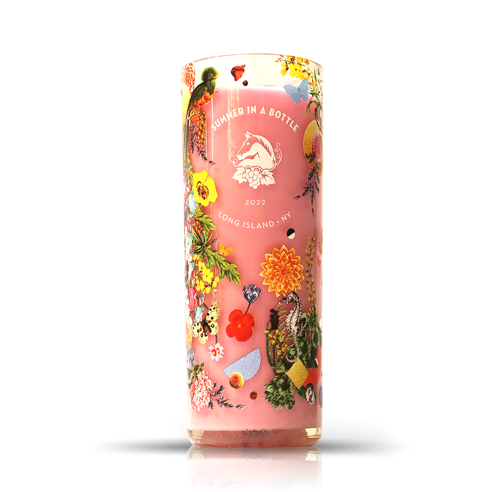 The Recycled Summer Pink Wine Candle is a tall upcycled bottle candle featuring a “Summer in a Bottle 2022 Long Island, NY” label with colorful floral and fruit designs on a pink background.