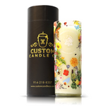 The Recycled Summer White Wine Candle, featuring colorful floral and animal designs in a white upcycled glass bottle, stands beside a black cylindrical "Custom Candle Co." box displaying contact details.