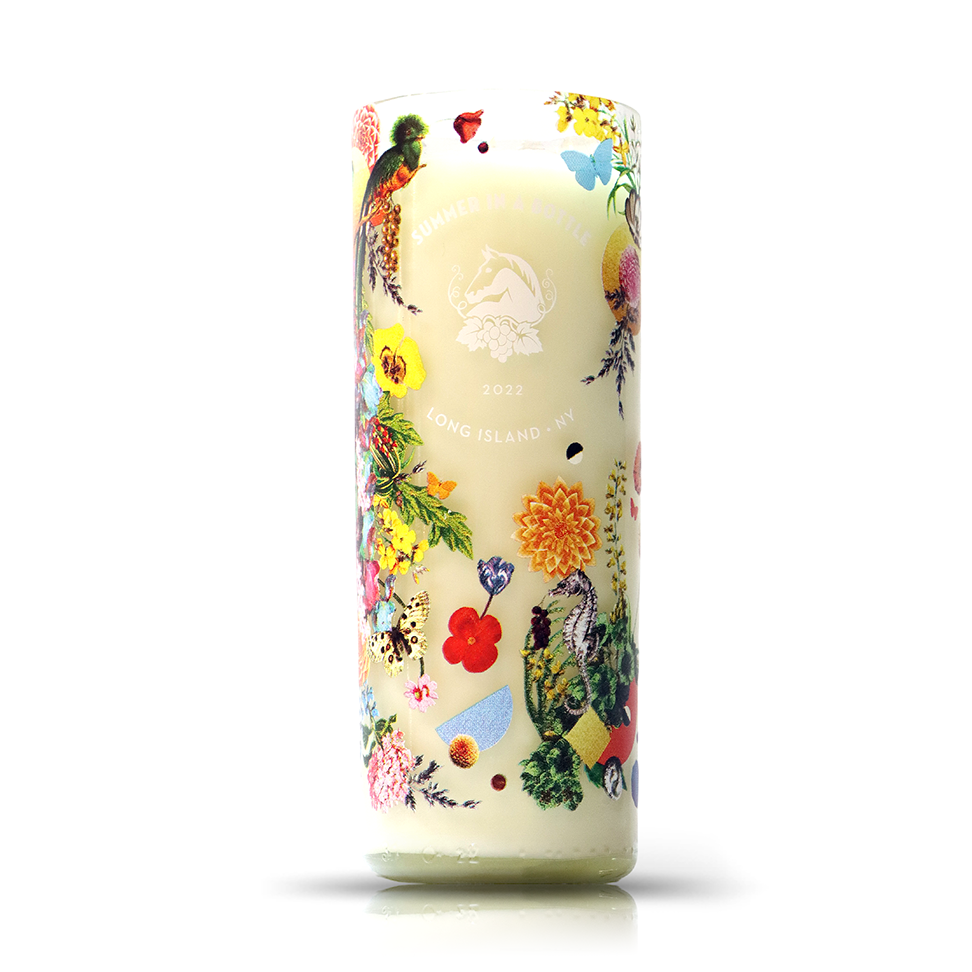The Recycled Summer White Wine Candle is a tall white candle in an upcycled bottle, featuring colorful flowers, birds, and butterflies with "SUMMER IN MONTAUK 2022 LONG ISLAND, NY" text. Eco-friendly and perfect for any décor.