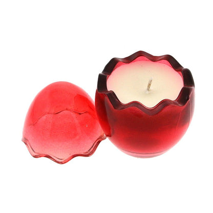 The Red Glass Easter Egg is a red, round, egg-shaped candle holder with a cracked egg design, containing a white natural wax candle inside and its lid placed beside it.