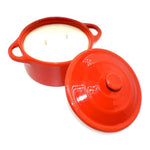 The Red Ceramic Dutch Oven Candle – Banana Nut Bread Scent features a two-handled red ceramic vessel holding a two-wick white soy wax candle, with the matching lid resting nearby.