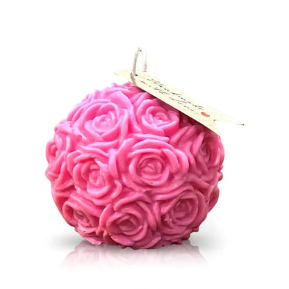 The Pink Pastel Rose Candle, featuring a round shape, pink hue, delicate rose pattern, and a small tag on the wick, is displayed against a white background.