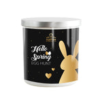 The Hello Spring White Tumbler Candle features gold "Hello Spring Egg Hunt" text and a bunny with hearts—making it a charming hand-poured candle for the season.