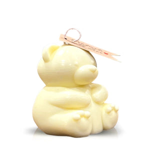 The Teddy Bear Pastel Yellow Chubby Candle is a cream-colored bear candle shaped like a sitting teddy bear, made from natural wax, and features a tag attached to the top.