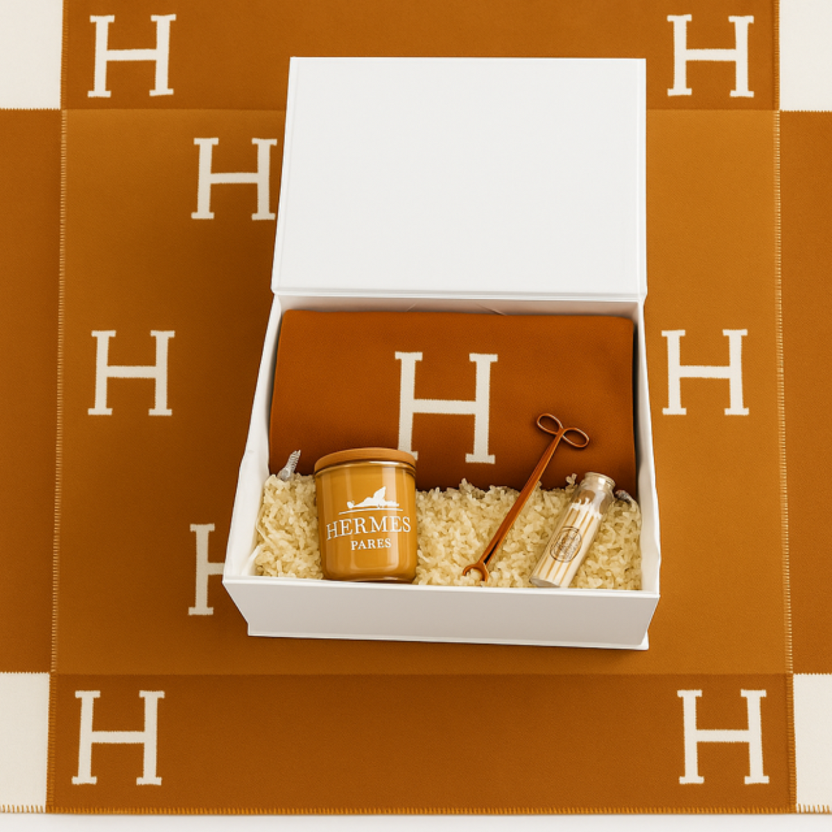 The Orange Paris Designer Gift Set includes a Hermes orange cotton throw, scented candle, gold key, and perfume vial—beautifully arranged on an orange Hermes blanket with white "H". Ideal for custom baskets or luxury gifts.