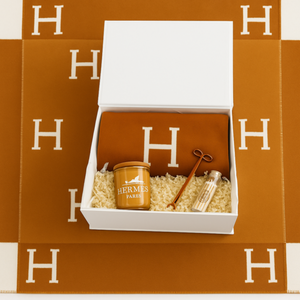 The Orange Paris Designer Gift Set includes a Hermes orange cotton throw, scented candle, gold key, and perfume vial—beautifully arranged on an orange Hermes blanket with white "H". Ideal for custom baskets or luxury gifts.