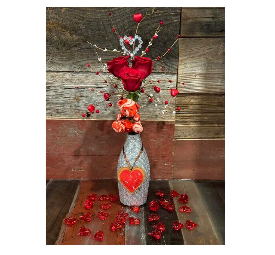 Valentine Bouquets feature red roses and heart-themed accents in a repurposed vase, with red heart ornaments on a wooden surface—a beautiful, eco-friendly Valentine’s Day gift.
