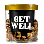 The "Get Well" Candle Gift Box Set features a natural wax candle with "GET WELL" in bold white letters on a black label, placed in a clear container with a gold lid and brown paper shreds—an ideal thoughtful gift.