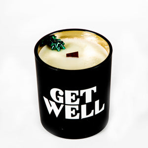 The "Get Well" Candle Gift Box Set includes a black holder with "GET WELL" in white lettering, a cream-colored natural wax candle, and a small green decorative accent—perfect for a thoughtful get well gift.