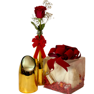 The Valentines Luxourious Gift Set – Gold Shiney Set features a red rose in a gold vase, a gold decorative piece, and a clear gift box with a champagne-scented candle and treats for an elegant, luxurious arrangement.