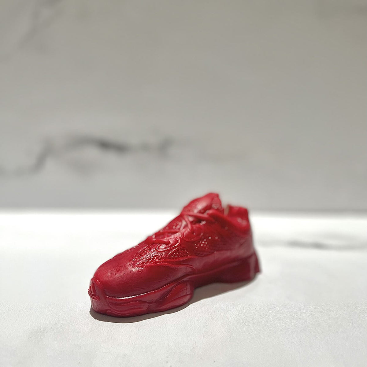 The Y500 – Red Sneaker Candle – Large (currently on backorder), hand poured with Black Ice scent, rests on a smooth light surface with a blurred marble background.