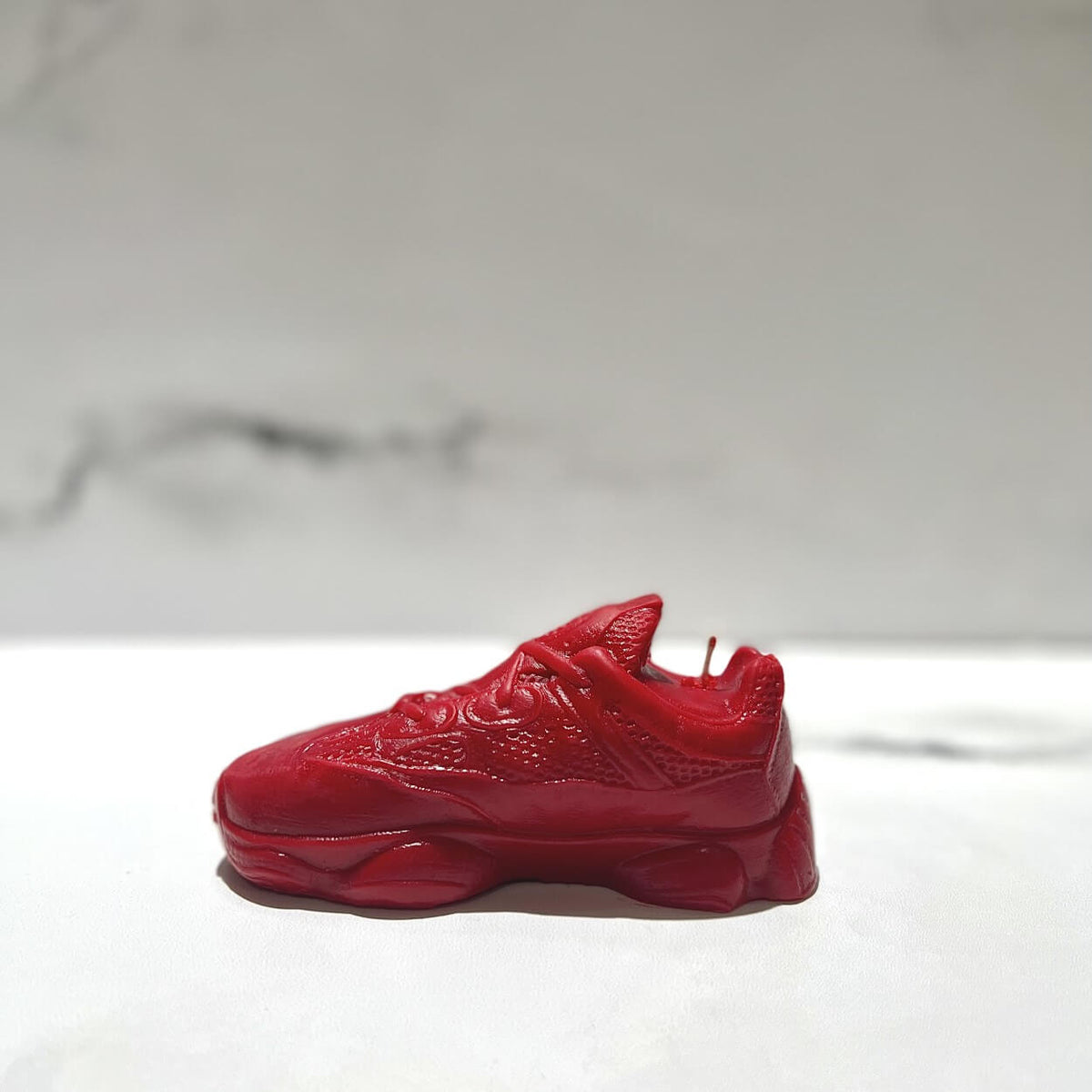 The Y500 – Red Sneaker Candle – Large (On Backorder) in vibrant red rests on a white surface against a neutral background, offering bold style and distinctive Black Ice scent.