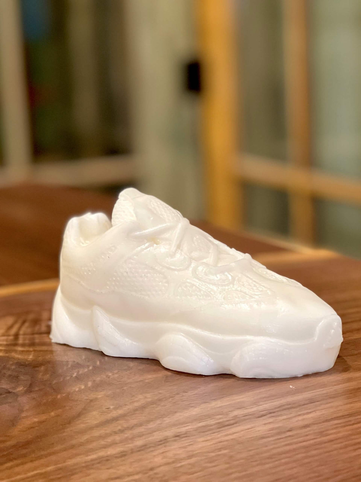 The Y500 – White Sneaker Candle – Large (On Backorder), hand poured and infused with Black Ice fragrance, rests on a wooden surface.
