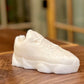 The Y500 – White Sneaker Candle – Small (On Backorder) is a realistic, hand-poured white sneaker candle infused with Black Ice fragrance, displayed on a wooden surface against a blurred background.