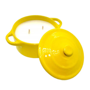 The Yellow Ceramic Dutch Oven Candle – Banana Nut Bread Scent features a yellow ceramic vessel with two handles, filled with white soy wax and two wicks, while its matching lid rests beside it.