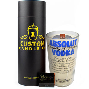 The Recycled Blue Letter Vodka Candle, made from a repurposed Absolut Vodka bottle, is displayed with a black cylindrical Custom Candle Co. box and a matching small black matchbox.