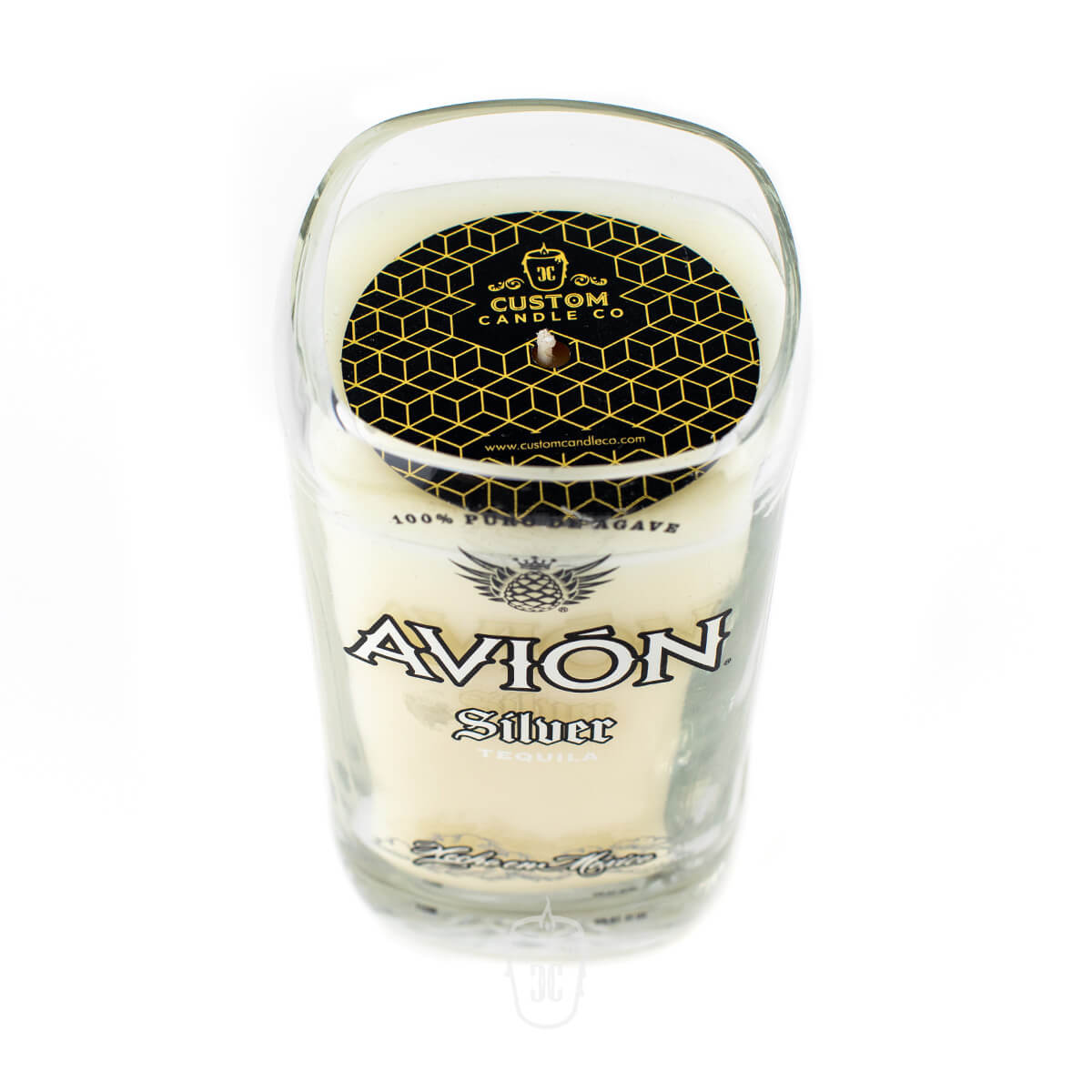 The Recycled Mexican-Style Silver Tequila Candle is a white soy candle in a clear glass holder crafted from an Avión Silver Tequila bottle, topped with a black and gold geometric-patterned lid—adding unique style to any space.
