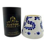 A black "Recycled Azul Tequila Candle" stands beside a white holder with blue floral patterns, showcasing a hand-poured, cruelty-free soy candle that's both sustainable and elegant.