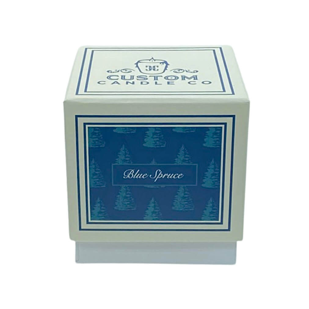 A square box labeled "Custom Candle Co" displays a blue panel with tree art and “Blue Spruce,” presenting the Holiday Scented Boxed Candle – Blue Spruce Scent for a festive, cozy vibe.