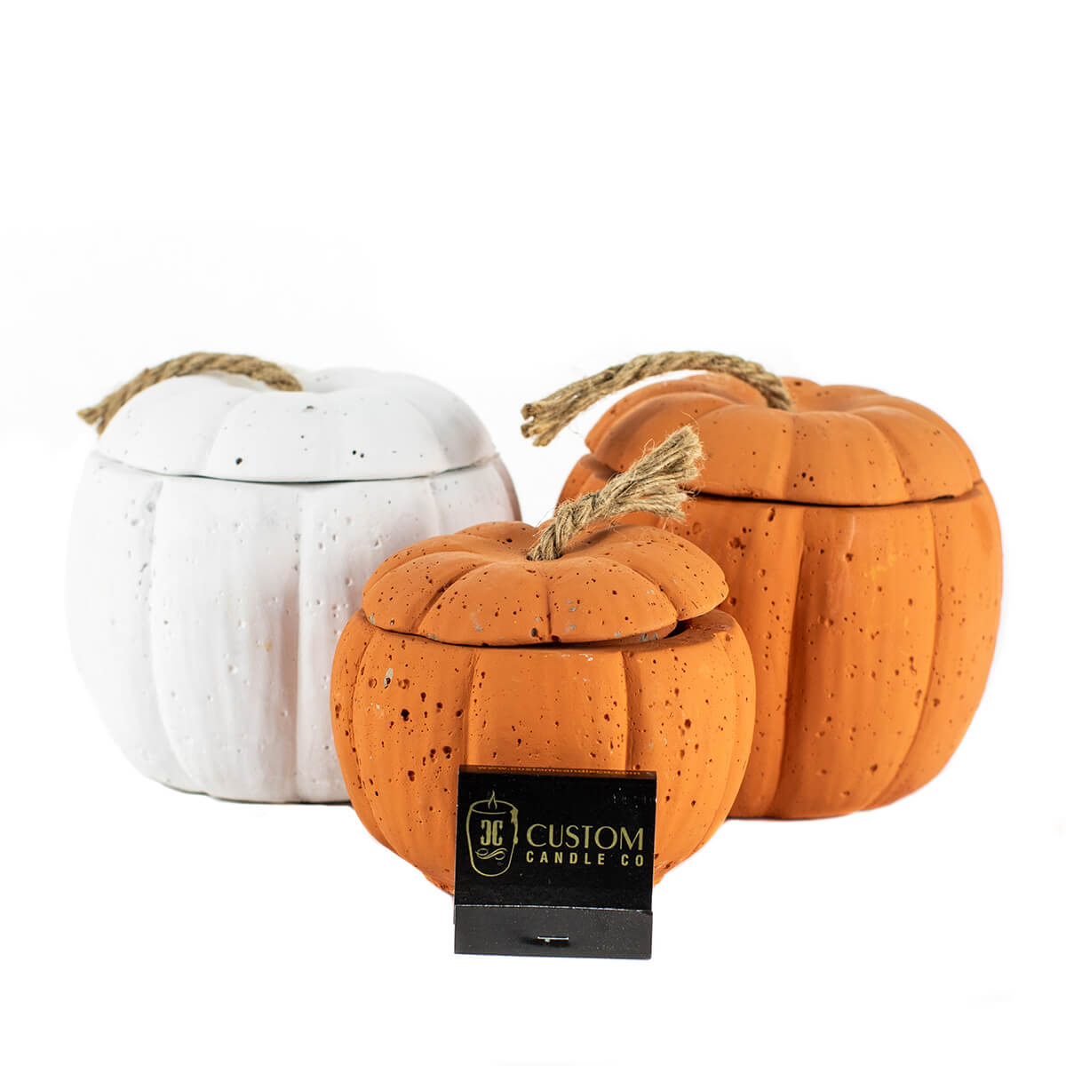 Add a custom touch to your decor with the White Cement Pumpkin Candle—one white and two orange, each pumpkin-shaped with rope-handled lids and "Custom Candle Co" tag.