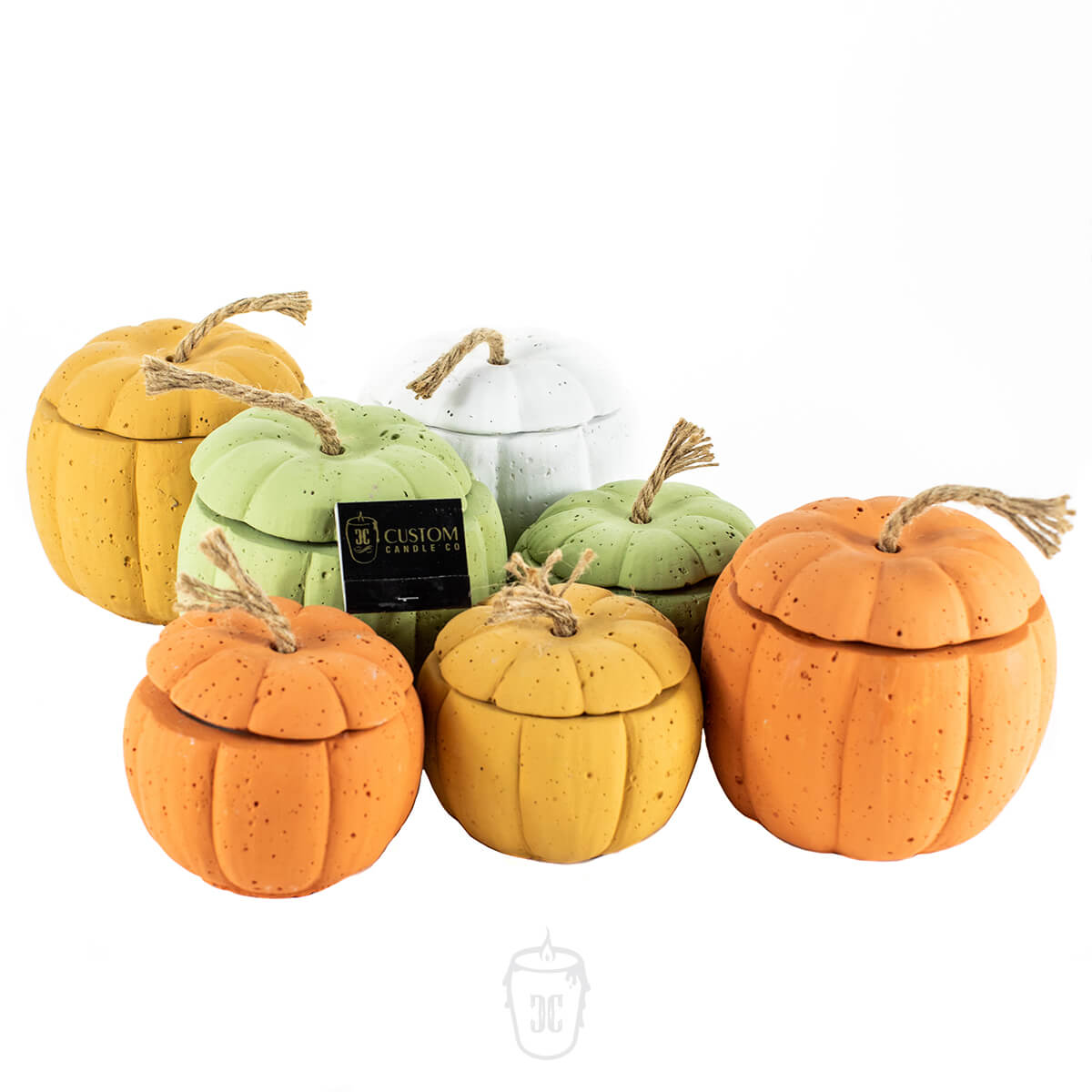 A group of yellow cement pumpkin candles with rope stems, in various sizes and colors, including orange, green, and white, are displayed together on a white background.