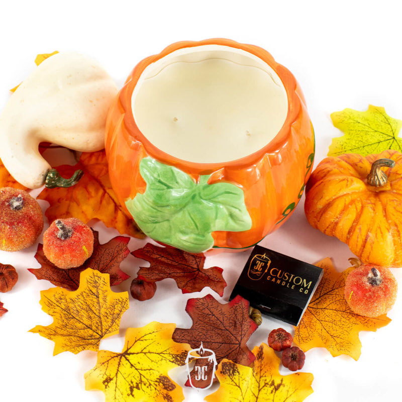 The Ceramic Large Leaf Pumpkin Candle, paired with artificial autumn leaves, small pumpkins, berries, and a Custom Candle Co. matchbox, sets a cozy scene—ideal for highlighting pumpkin spice or your favorite soy candle fragrance.
