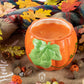 The Ceramic Large Leaf Pumpkin Candle with three wicks and a pumpkin spice scent sits on a cozy blanket, surrounded by autumn leaves, acorns, and festive fall decor.