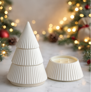 The White Ceramic Christmas Tree Candle, featuring a ribbed ceramic design and an all-natural hand-poured wax interior with its lid off, sits beside softly glowing holiday lights and festive decorations in the background.